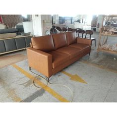 a brown leather couch sitting on top of a floor next to a pile of chairs