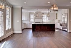 an empty kitchen with wood floors and white cabinets in the center, along with large windows