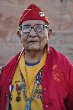 an old man with glasses and a red jacket is standing in front of a rock wall