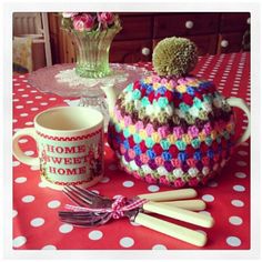 a crocheted tea pot, mug and spoons on a table with polka dots