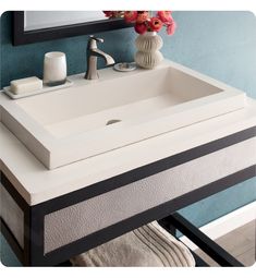 a bathroom sink sitting under a mirror next to a vase with flowers on top of it