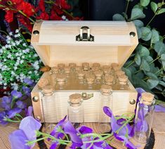 a wooden box filled with lots of bottles next to purple flowers and greenery in the background