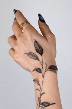 a woman's hand with black nail polish holding a flower tattoo on her left wrist