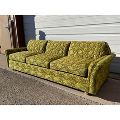 a green couch sitting in front of a white building with a garage door behind it