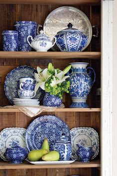 blue and white china is on display in a hutch with flowers, pears and other items