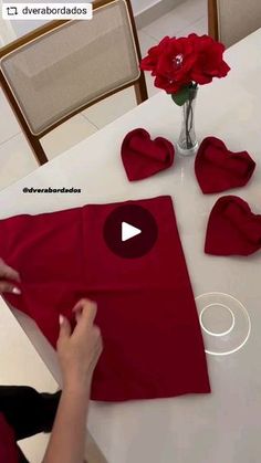 a woman is making heart shaped napkins on a table with flowers in a vase