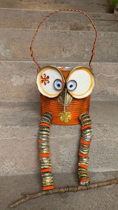 an owl made out of tin cans sitting on top of some steps with beads around its eyes