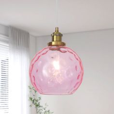 a pink glass ball hanging from a ceiling light in a room with white walls and windows