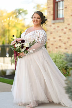 a woman in a white dress holding a bouquet and posing for the camera on her wedding day