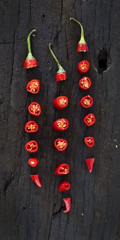 several red peppers are arranged on a piece of wood with one pepper still attached to the other