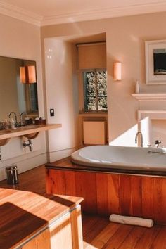 a large bath tub sitting on top of a wooden floor next to a mirror and fireplace