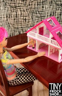 a doll house sitting on top of a wooden table next to a woman's hand