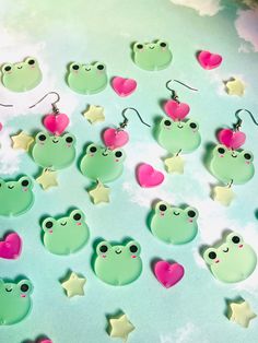 frog earrings with heart shaped eyes and stars on the earring hooks are shown against a blue background