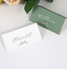 two place cards sitting on top of a table next to some flowers and greenery