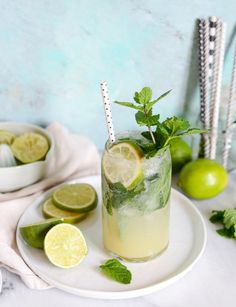 a mojito with limes and mint on a white plate next to silver straws