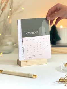 a calendar is being held up on a desk next to a pen and christmas tree