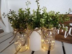 two mason jars with lights and greenery in them