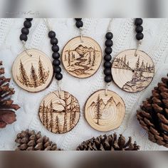 four wood burned ornaments with pine cones and beads on a white tablecloth, surrounded by pine cones