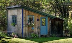 a small wooden shed sitting in the middle of a lush green field next to trees