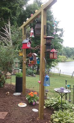 a bird feeder stand in the middle of a garden with lots of birds hanging from it's roof