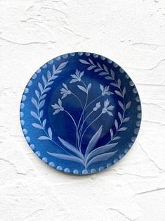 a blue and white plate with leaves on the rim is hanging on a stucco wall