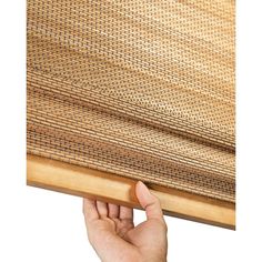 a hand is holding up the edge of a bamboo window covering that's partially closed