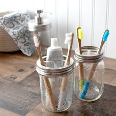 two mason jars filled with toothbrushes on top of a wooden table