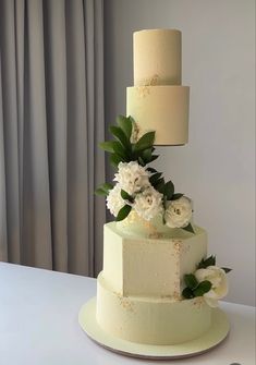 a three tiered cake with white flowers and greenery on the top, sitting on a table