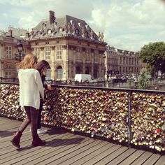 a woman is looking at her cell phone on the bridge covered in padlocks