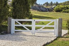 an image of a white gate in the middle of a stone path with grass and trees behind it