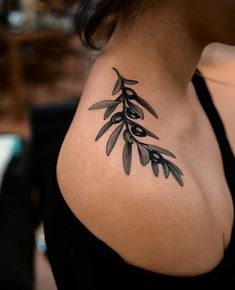 an olive branch tattoo on the back of a woman's shoulder