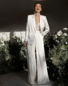 a woman standing in front of flowers wearing a white suit