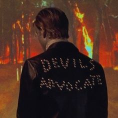 the back of a man wearing a jacket with words written on it in front of trees