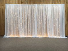 a white curtain with lights on it in front of a wooden wall and carpeted floor