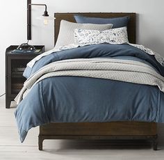 a bed with blue comforter and pillows in a white room next to a night stand