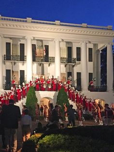 a group of people standing in front of a large white building with christmas decorations on it