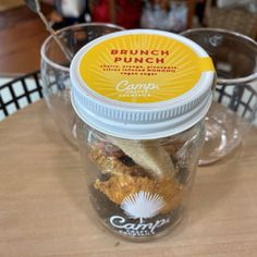 a glass jar filled with food sitting on top of a wooden table next to two plastic cups