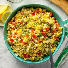 a bowl filled with corn and vegetables on top of a table next to sliced lemons