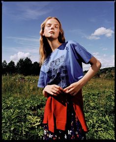 a woman standing in a field with her hands on her hips and looking off to the side