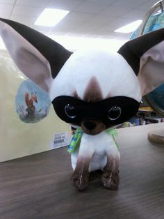 a small stuffed animal wearing a mask on top of a wooden table in an office