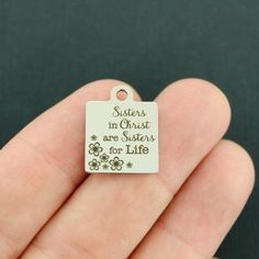 a hand holding a small white tag with words on it that says sisters in christ are sisters for life