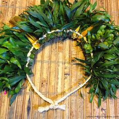 a wreath made out of green leaves on top of a bamboo mat with white string