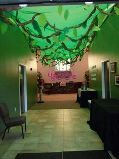 an empty room with tables and chairs in the center is decorated with green leaves hanging from the ceiling