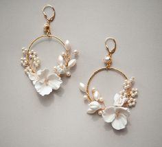 two pairs of earrings with flowers and pearls hanging from hoops on a white surface