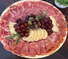 an assortment of meats, cheese and olives on a platter with grapes