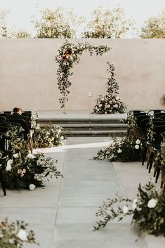 an outdoor ceremony setup with flowers and greenery on the aisle, surrounded by black chairs