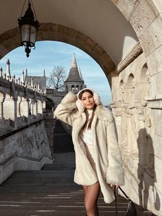 a woman is walking down the stairs with her hand in her hair and wearing a fur coat