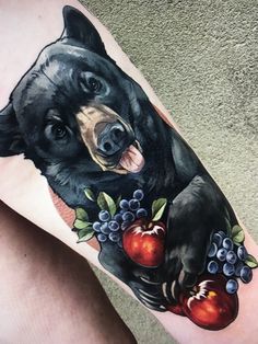 a black bear with apples and grapes on his leg is shown in this tattoo design