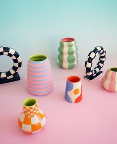 several different colored vases sitting on a pink surface