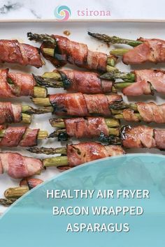 bacon wrapped asparagus on a white platter with text that reads healthy air fryer bacon wrapped asparagus